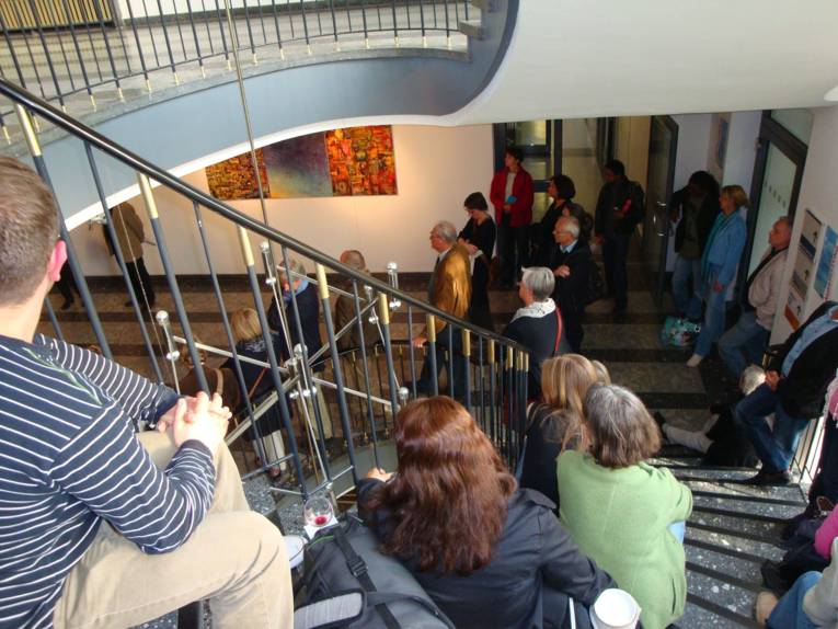 Viele Personen stehe in einem Treppenhaus oder sitzen auf den Treppenstufen.